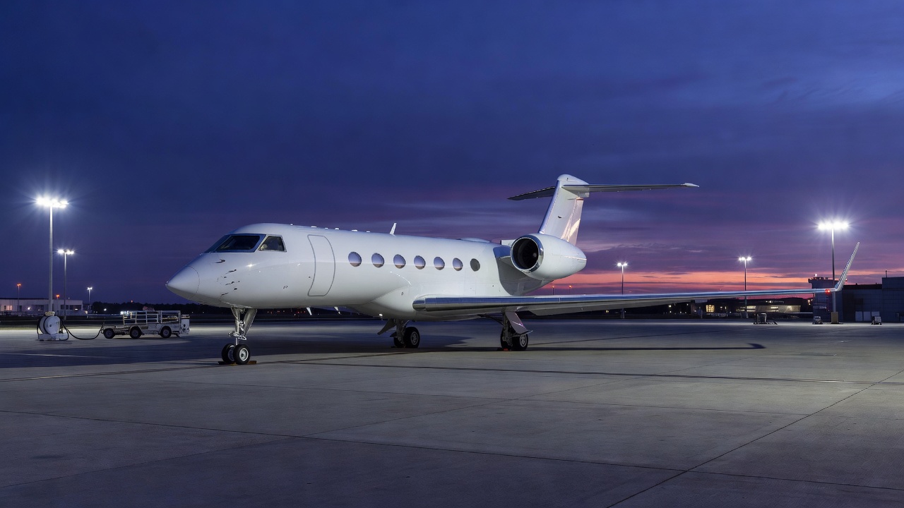 A business aircraft parked on a well-lit airport apron during evening twilight